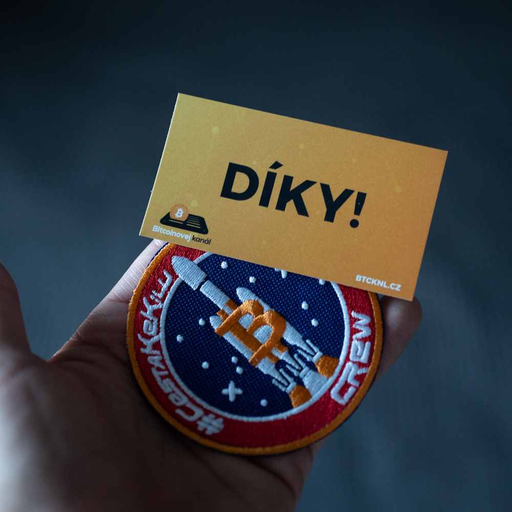 Ruka drží kartičku s nápisem DÍKY! a nášivku
