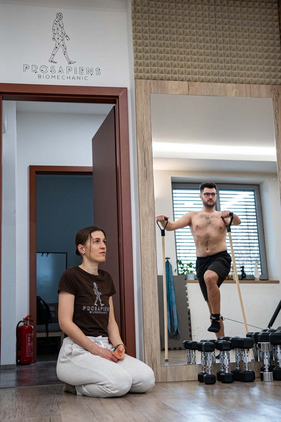 Klient při cviku, trenérka sleduje z podlahy