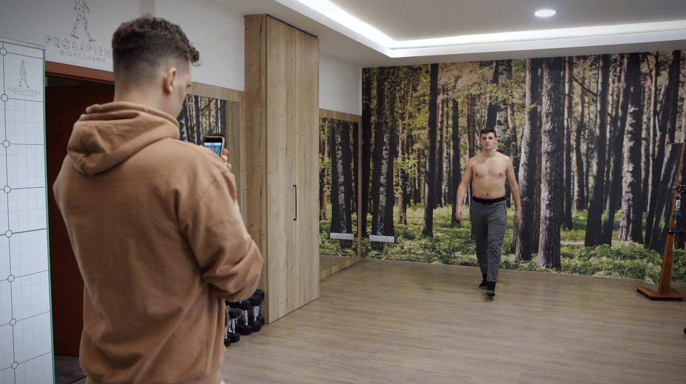 Trenér natáčí chůzi klienta telefonem při analýze pohybu